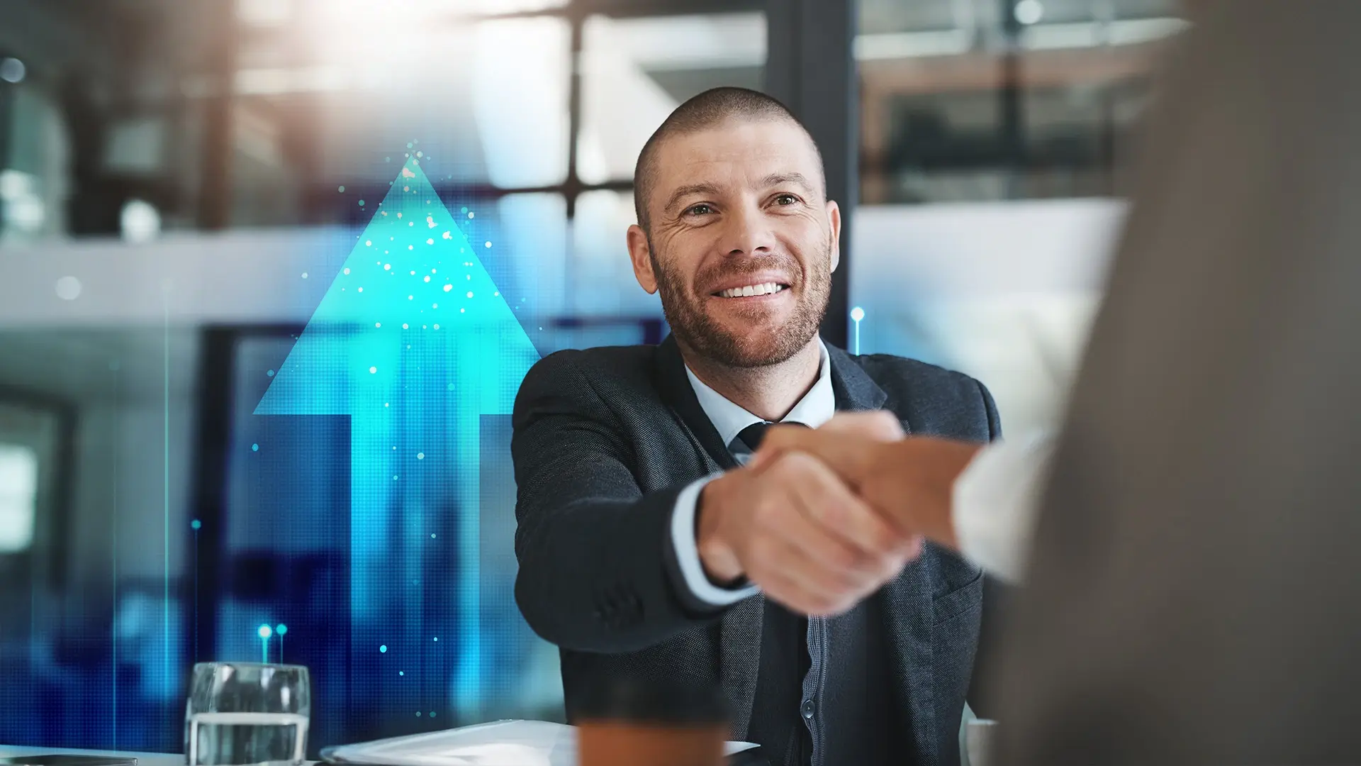 Smiling businessman in a suit shaking hands with a colleague, with a blue upward arrow graphic in the background, symbolizing growth and success.